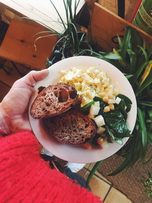 Une assiette tenue à la main : tartines de pain au levain, feta et épinards