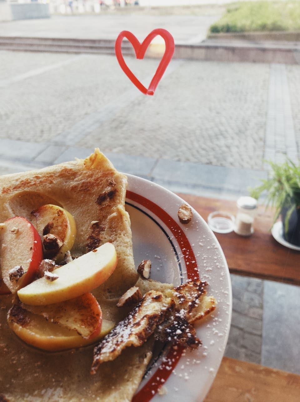 Une crêpe garnie de tranches de pomme, de noix et de sirop, servie près de la fenêtre