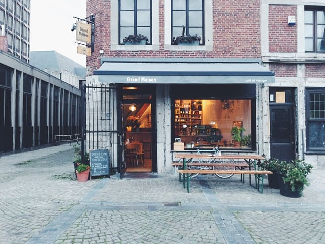 La façade du café depuis la place, vitrine éclairée et banc devant l'entrée